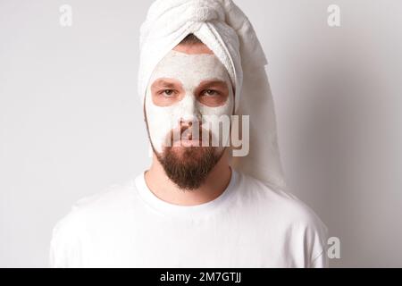 Man in white tshirt apply facial mask stand against white background. Self care morning spa procedure Stock Photo