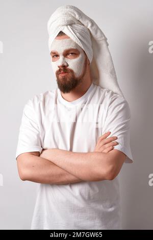 Man in white tshirt apply facial mask stand against white background. Beauty treatment, grooming and wellbeing concept Stock Photo