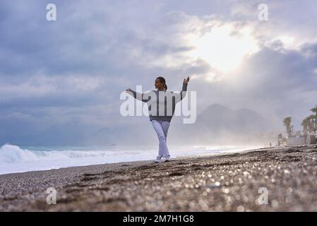 Young woman on the sand beach and watching the sea waves. Stock Photo
