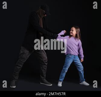 Terrorist and scared little hostage on dark background Stock Photo