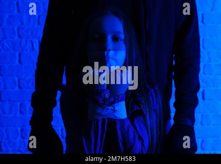 Terrorist and scared little hostage on brick background Stock Photo