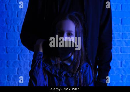 Terrorist and scared little hostage on brick background Stock Photo