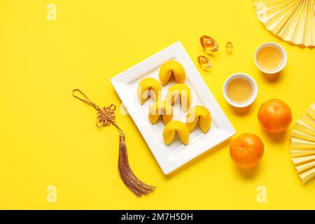 Plate with fortune cookies, mandarins, cups of tea and Chinese symbols on yellow background. New Year celebration Stock Photo