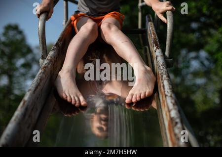 Kid at top of metal slide on playground in summer Stock Photo