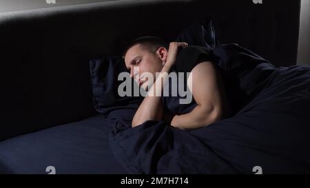 Disturbed sleep. I have nightmares. The young guy tosses and turns in bed Stock Photo