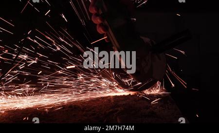 bright sparks from a circular in the dark on a black background close-up. A worker cuts metal with a circular saw close-up. Working with iron. Stock Photo