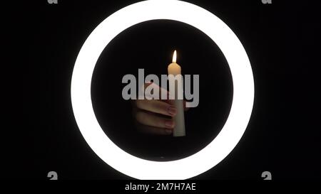 female hands light a candle close-up on a black background. burning fire on a candle stick. The concept of ritual actions. Stock Photo