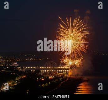 Firework display over Eastbourne, East Sussex with the illuminated pier in the background and the light of the fireworks reflected in the sea Stock Photo