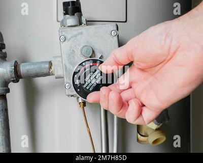 Plumber adjusting thermostat temperature dial on natural gas hot water heater. Residential boiler tank controls for heating household water. Stock Photo