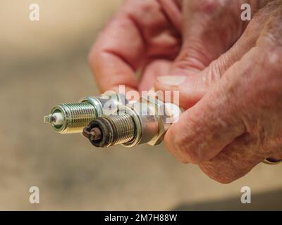 Mechanic holding new and used spark plugs. Replacing worn out automotive gas engine electrodes. Stock Photo