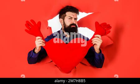 Bearded man with red heart looking through hole. Businessman in stylish shirt with love symbol. Stock Photo