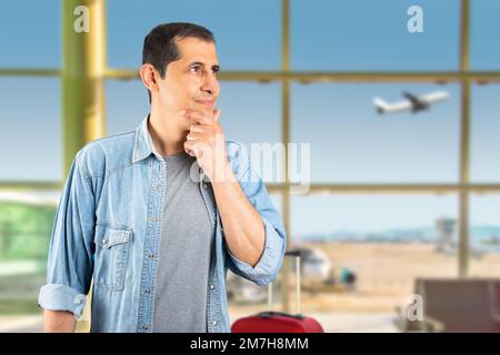 Man wearing casual blue shirt at airport with hand on chin thinking about question, pensive expression. Smiling with thoughtful face. Doubt concept. Stock Photo