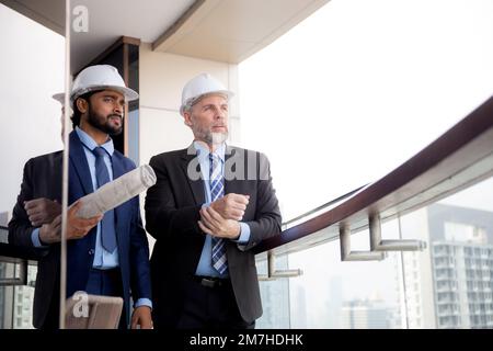 Senior architect inspector talking with contractor man together at office while holding blueprint building structure, executive and engineer planning Stock Photo