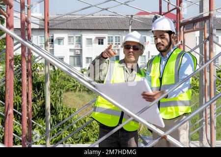 Two young architect discussion or contractor man while looking blueprint building structure together for survey on construction site, engineer plannin Stock Photo
