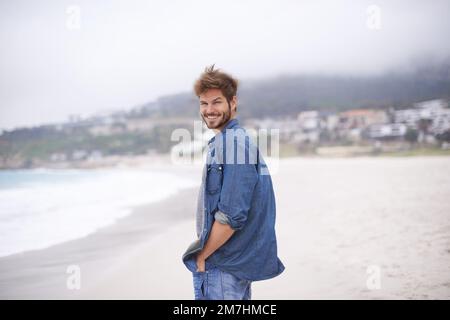 Enjoying the therapeutic feelings of the sea. a young man enjoying a day at the beach. Stock Photo