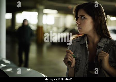 Ive got to get away from here. A terrified young woman in an underground parking garage being followed by a sinister man. Stock Photo