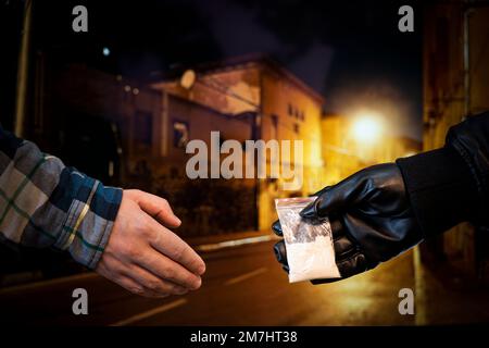 Drug dealer selling junkie. Man hand holds plastic packet or bag with addict narcotics cocaine powde, drug dealer sale and danger addiction overdose c Stock Photo