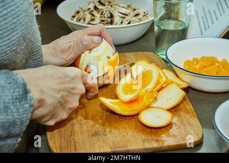 Chef cuts oranges to prepare salad with zucchini, oranges and salami. French gourmet cuisine, on a wooden background. Stock Photo