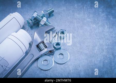 Adjustable spanner bolt washers nuts bolts and rolls of construction drawings on metallic background top view maintenance concept. Stock Photo