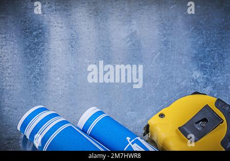 Blue rolled construction drawings measuring tape on metallic background. Stock Photo