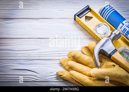 Claw hammer blue rolled construction plans level safety gloves on wooden board. Stock Photo