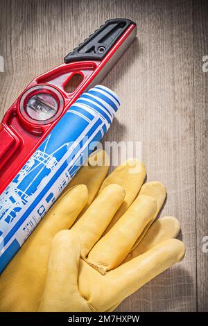 Composition of safety gloves construction level blue rolled engineering drawings on wooden board. Stock Photo