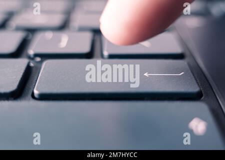 Man's hand on notebook keyboard on a light background. guy presses the enter button on the black keyboard of modern ultrabook. Stock Photo