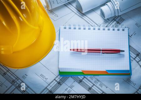 Hard hat checked notebook pen blueprints on construction drawing. Stock Photo