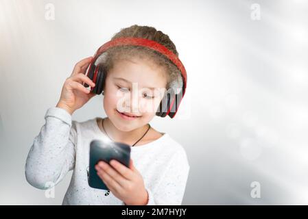 A beautiful little girl listens to music on headphones, holds a phone in her hands. generation concept Stock Photo
