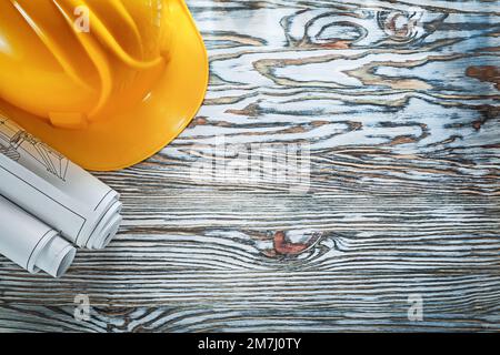 Rolled construction plans building helmet on vintage wooden board. Stock Photo