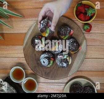 hands take a chocolate eclair served on a wooden tray Stock Photo