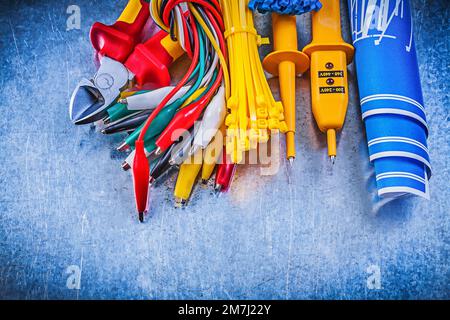 Yellow electrical tester crocodile plugs cable ties blue construction plans nippers on metallic background electricity concept. Stock Photo