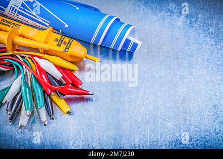 Yellow electrical tester crocodile cables set blue construction plans on metallic background electricity concept. Stock Photo