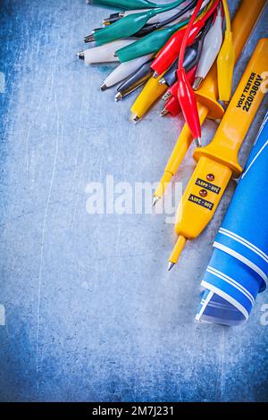 Yellow electrical tester crocodile cables set blue blueprints on metallic background electricity concept. Stock Photo