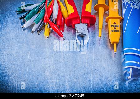 Yellow electrical tester crocodile cables set blue construction drawings nippers on metallic background electricity concept. Stock Photo