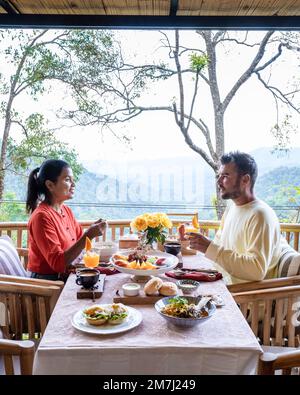 A Couple have breakfast outdoor, luxury breakfast in the mountains of Chiang Mai Thailand, luxury breakfast with Chiang Mai curry noodle soup or Khao Soi Gai and fruits and coffee on the table.  Stock Photo