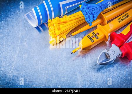 Yellow electrical tester self-locking cable ties blue blueprints nippers on metallic background electricity concept. Stock Photo