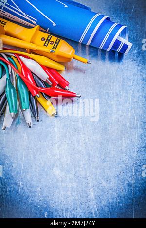 Yellow electrical tester crocodile cables set blue construction drawings on metallic background electricity concept. Stock Photo