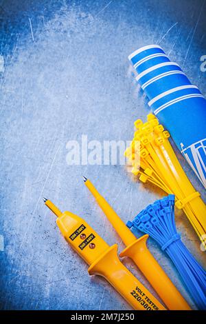 Yellow electrical tester self-locking cable ties blue construction plans on metallic background electricity concept. Stock Photo