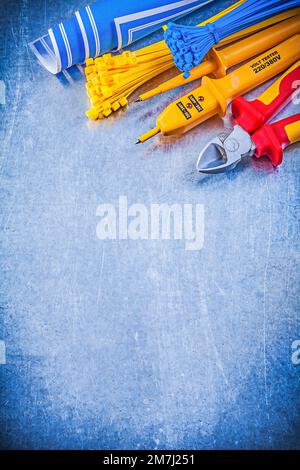 Yellow electrical tester self-locking tying cables blue blueprints nippers on metallic background electricity concept. Stock Photo