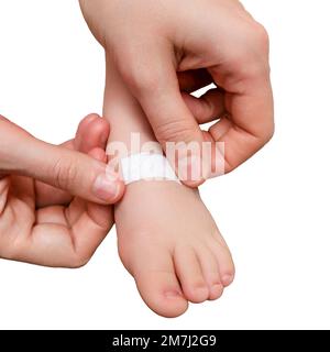 Mother woman sticks a medical adhesive plaster on the toddler baby leg, isolated on a white background. Mom s hand with sticky wound protection tape a Stock Photo