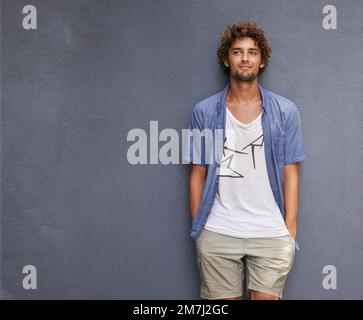 Cool and casual. A handsome young man leaning against a bluegray wall. Stock Photo