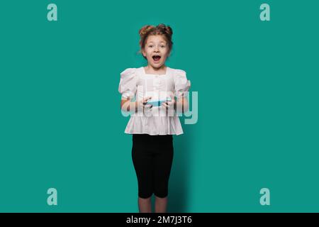 Photo portrait of amazed little girl browsing internet opened mouth and looking at camera isolated on blue color background. Stock Photo