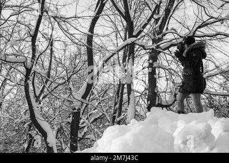 A grayscale of a female photographer standing on snow and taking photos Stock Photo