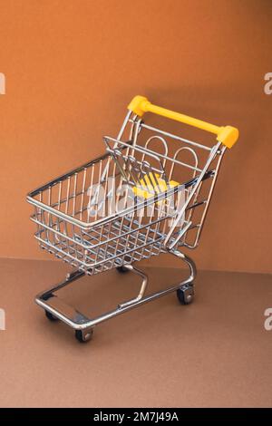 Empty shopping trolley cart on beige background. Copy space for your text. Online shopping, buy mall market shop consumer concept. Small toy supermarket grocery push cart. Food crisis. Rising food cost, grocery prices shortage mass hunger. Inflation Stock Photo