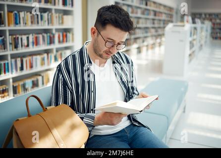 Education, man and student reading in library, knowledge and studying for exams, test and intelligent. Young male, guy and academic with book Stock Photo