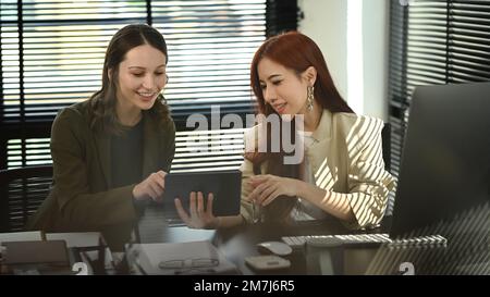 Smiling business coworkers looking at digital tablet and discussing over new business project at office Stock Photo