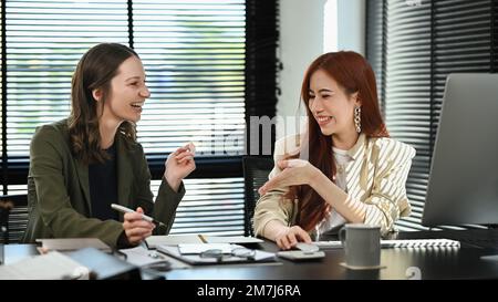 Two smiling businesswomen discussing over new business project and planning marketing strategy at corporate office Stock Photo