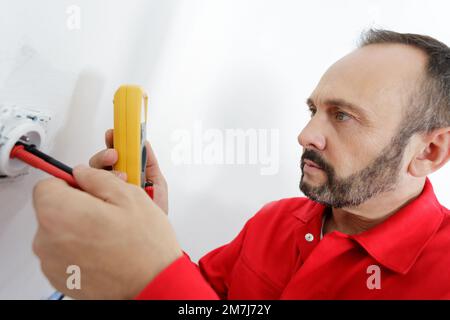 mature male electrician testing socket with multimeter Stock Photo