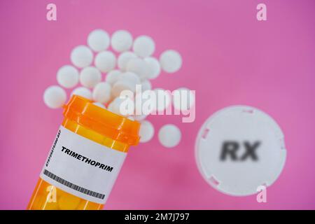 Trimethoprim Rx medicine pills in plactic vial with tablets. Pills spilling   from yellow container on pink background. Stock Photo